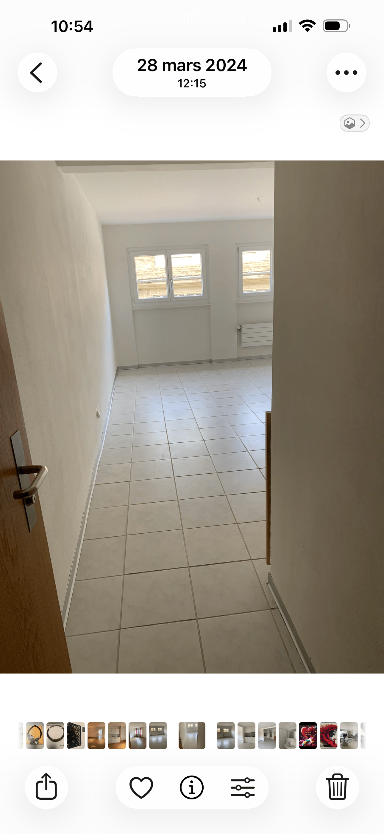 Empty room with white tiled floor and white walls, featuring two windows and a radiator.