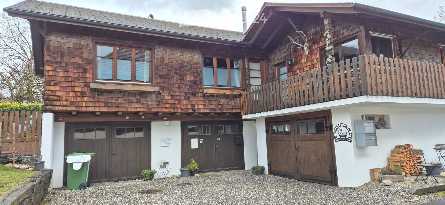Two-story wooden house with multiple garage doors, large windows, and a balcony on the upper level.