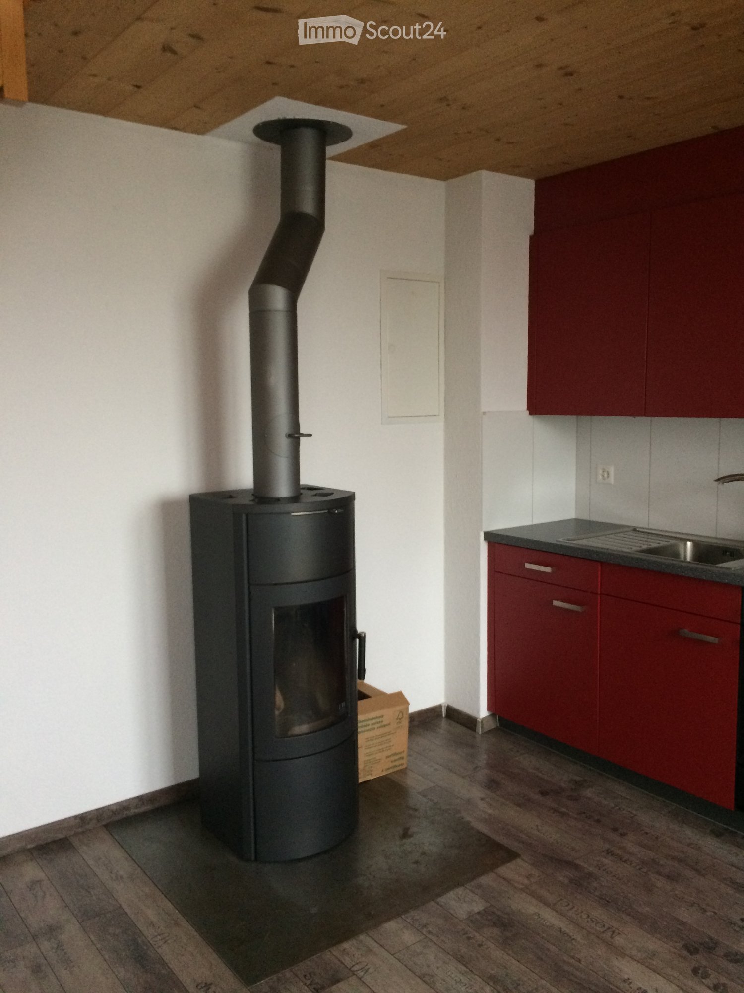 A room with a modern black wood-burning stove, red cabinets, and a sink.
