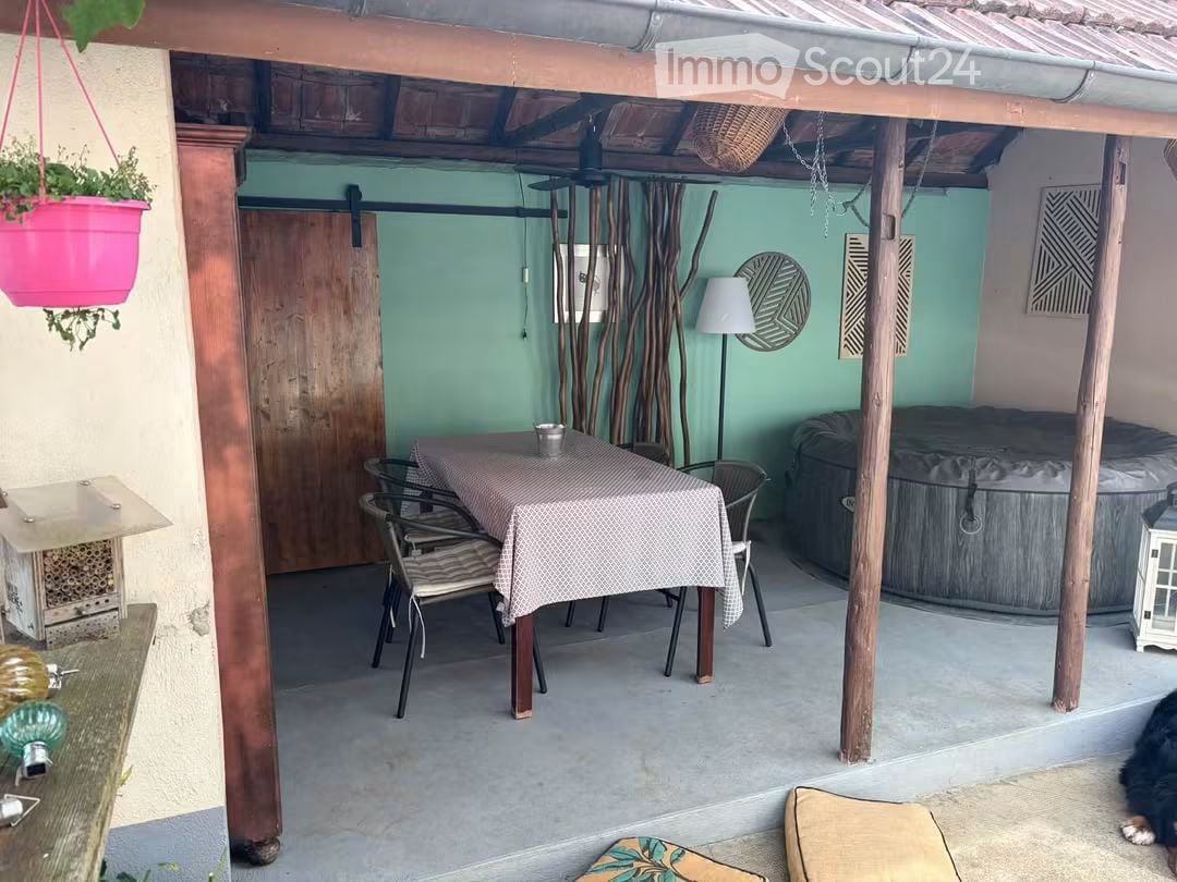 Outdoor patio area with a dining table, chairs, a hanging basket, a small lamp, and a hot tub.