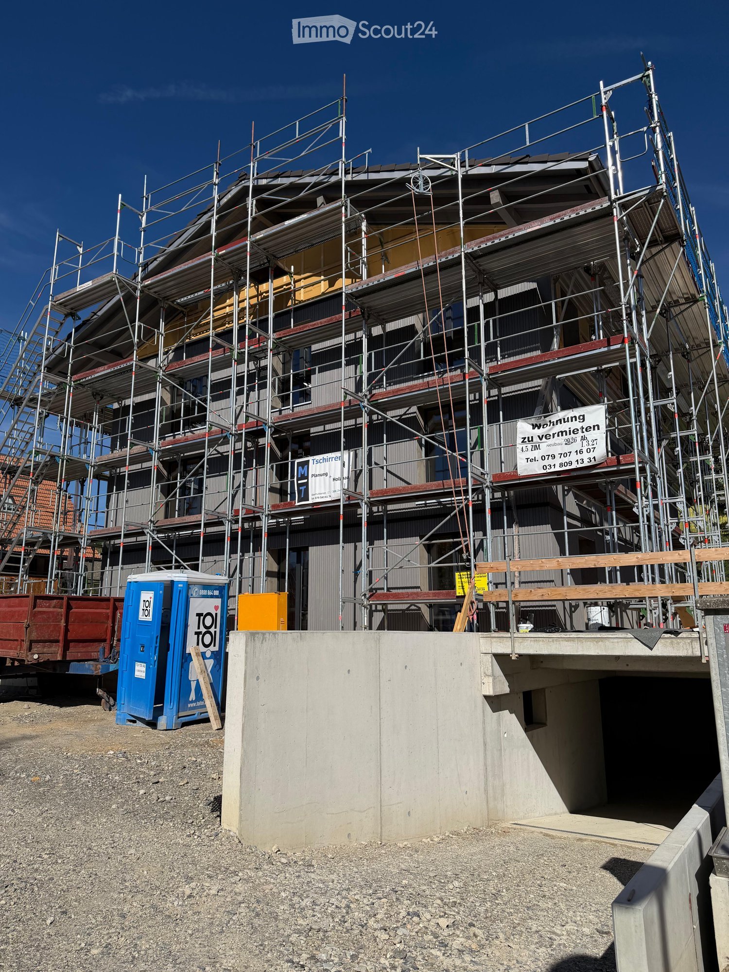 Multi-story building under construction with scaffolding, visible signage, and a portable toilet nearby.
