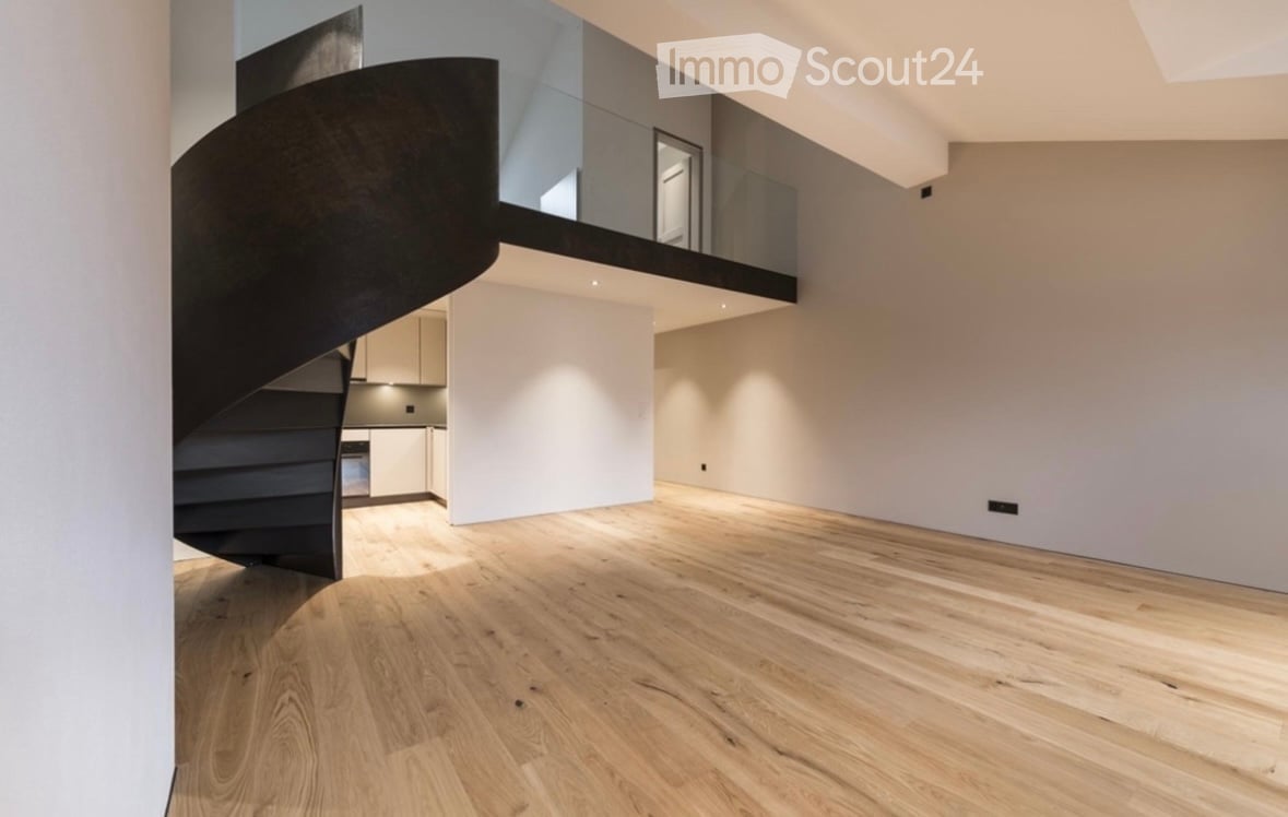 Open-plan space with light wooden flooring, white walls, and a modern black spiral staircase leading to an upper level with glass railing.