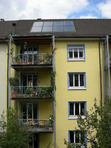 Yellow apartment building with multiple balconies, each decorated with potted plants and outdoor furniture.
