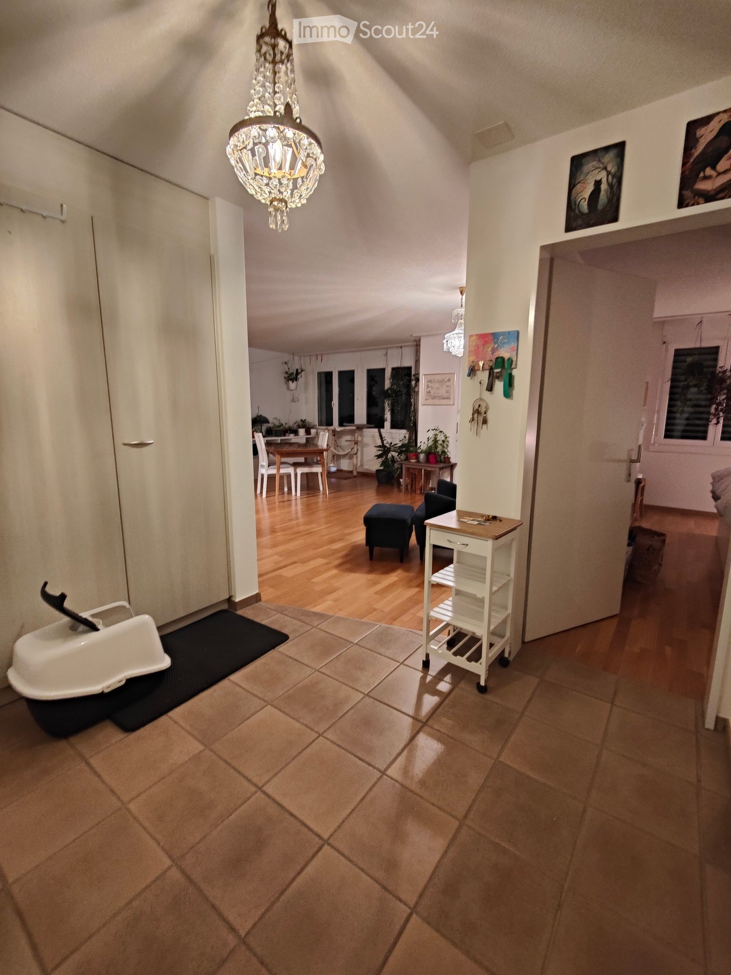 Hallway with tiled floor, wooden floor in adjacent rooms, chandelier, small table, and various furniture visible in connected spaces.