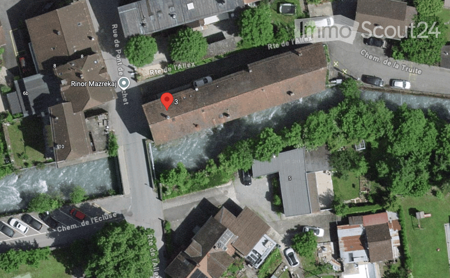 Aerial view of a residential area showing multiple buildings with red-tiled roofs, surrounded by greenery and streets.
