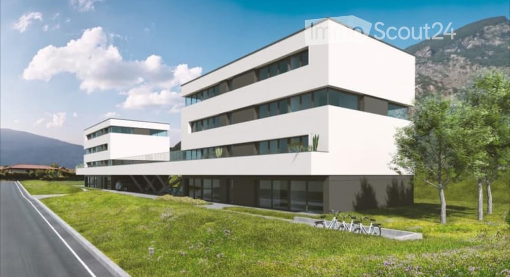 Modern, multi-story white building with large windows and a sleek design, surrounded by a green lawn and trees.