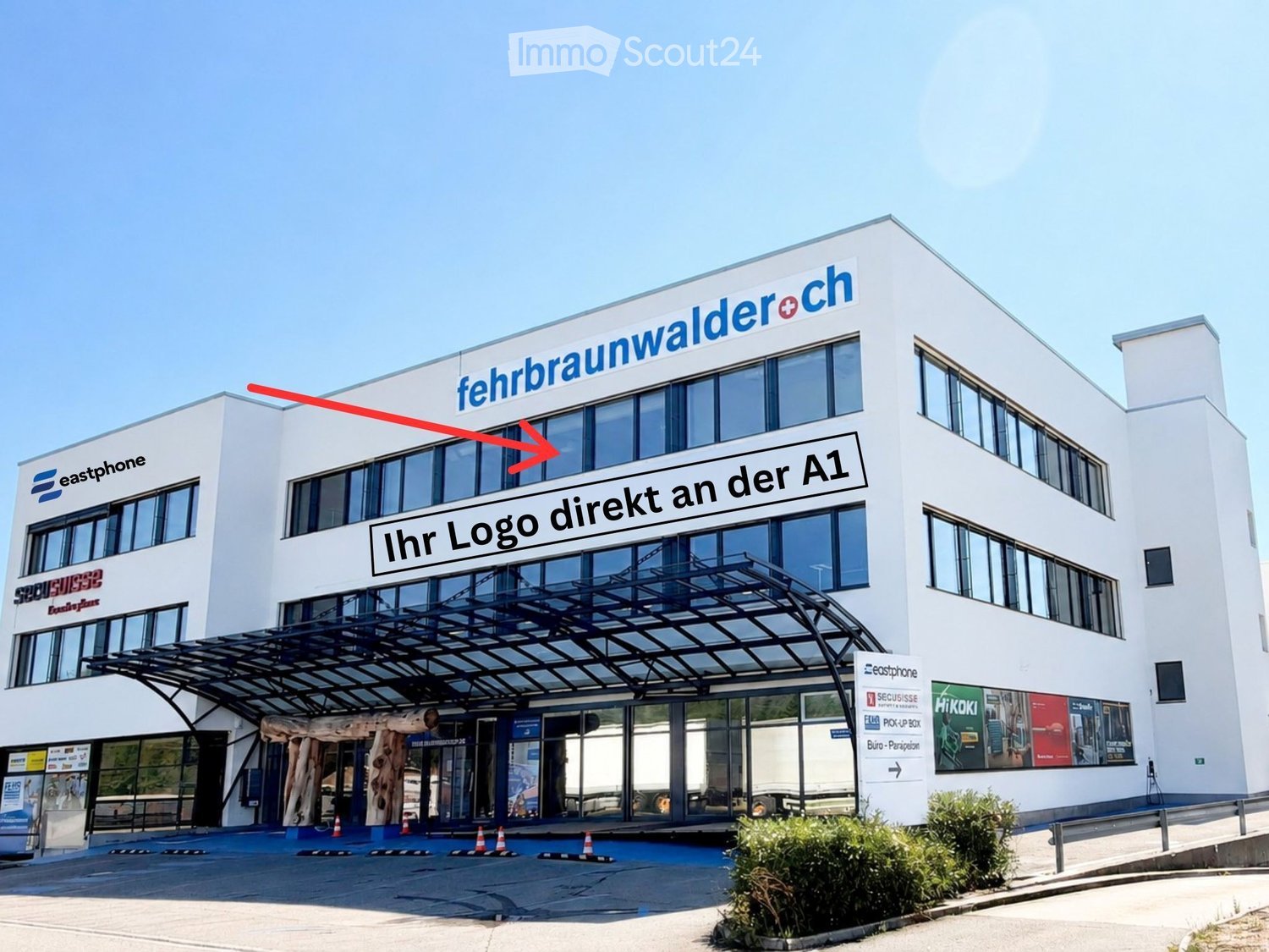 Modern multi-story building with large windows, signage for 'fehrbraunwalder+ch' and 'Ihr Logo direkt an der A1', a covered entrance area, and traffic cones in the foreground.