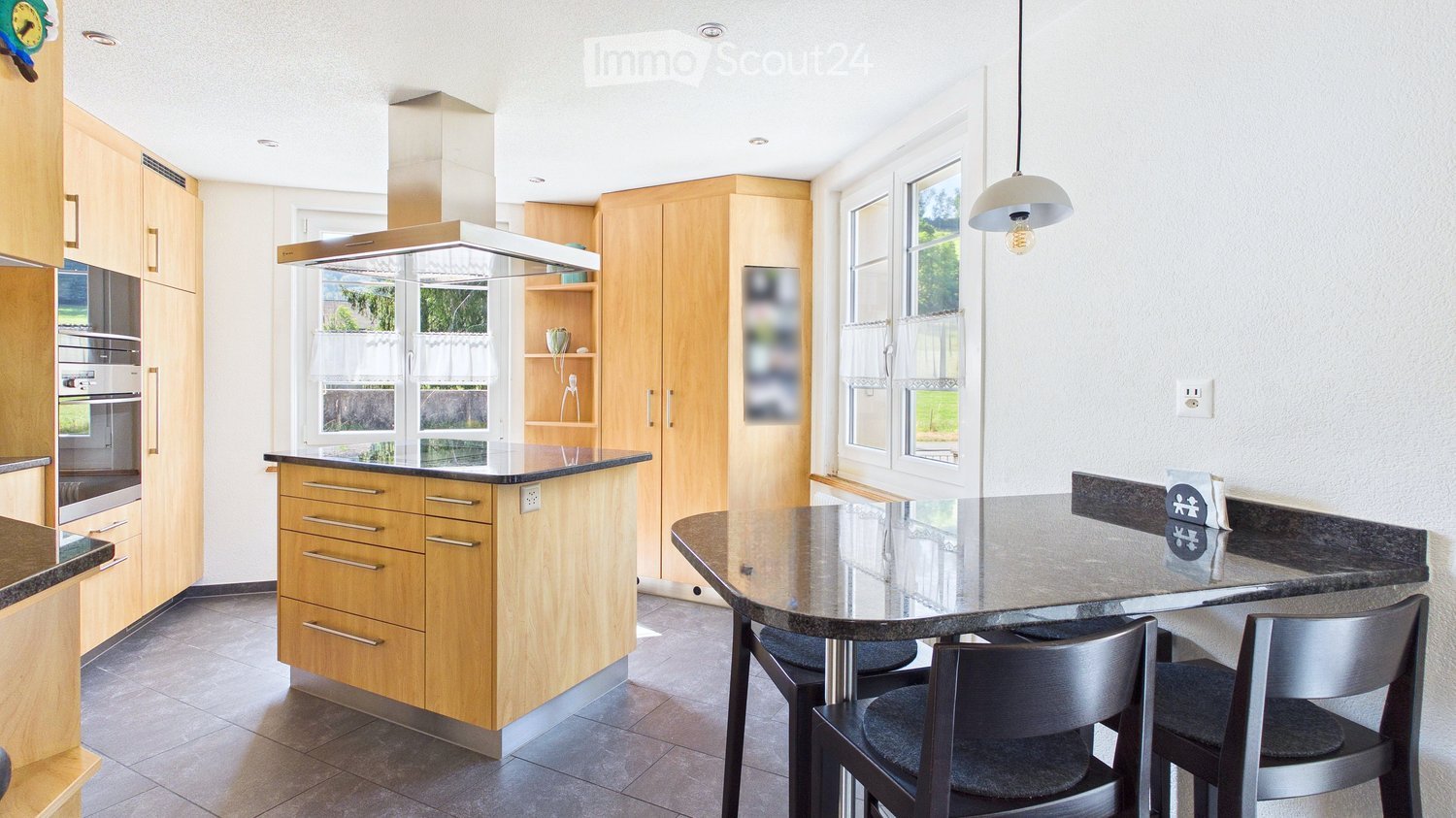 Modern kitchen with wooden cabinets, stainless steel appliances, island with seating, and pendant light.