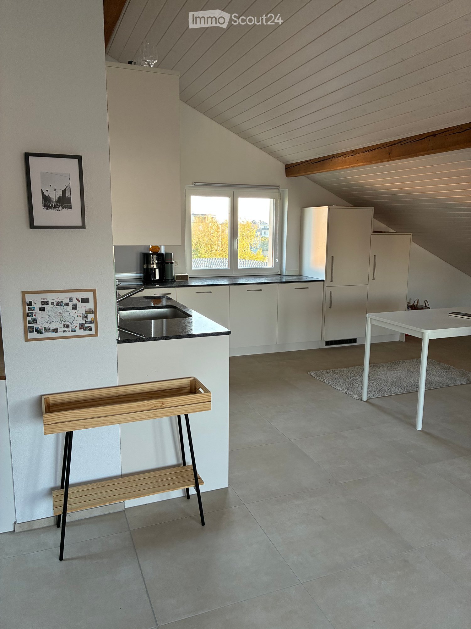 Modern kitchen with white cabinets, stainless steel sink, refrigerator, coffee maker, and a small wooden bench near the wall.