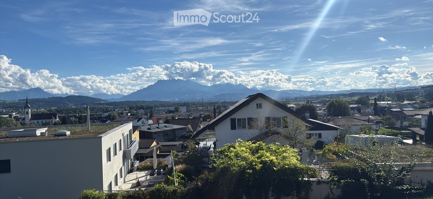 View of a town with houses, trees, and mountains in the background under a clear blue sky.
