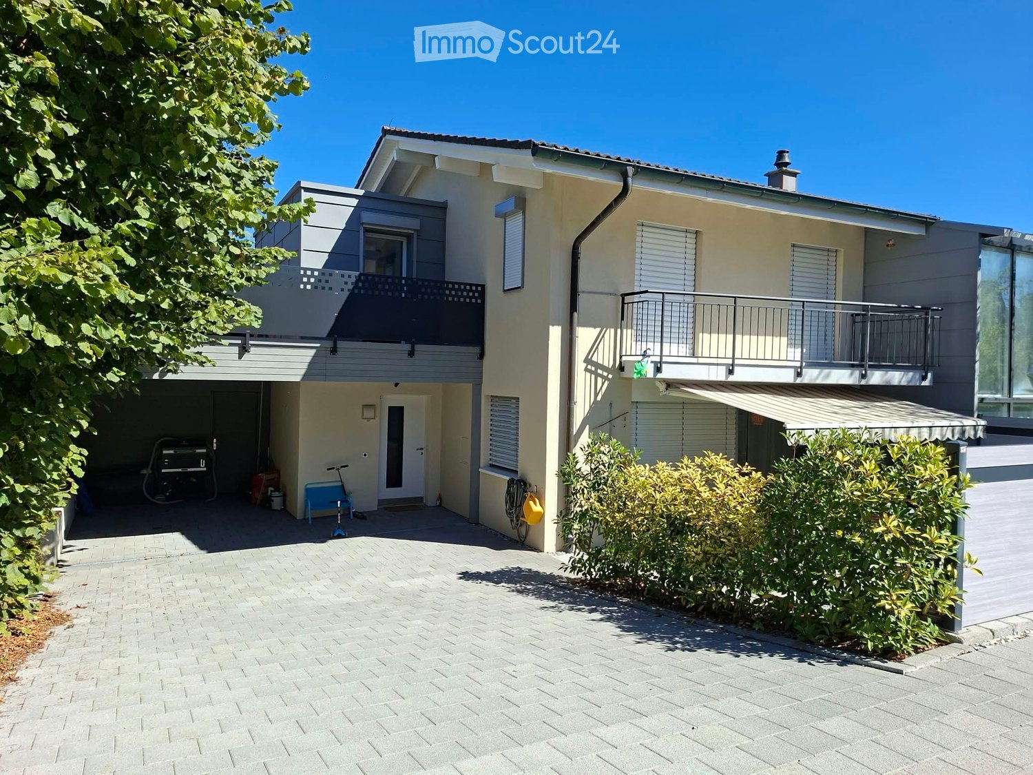 Two-story house with beige exterior, multiple windows, balconies, garage, and small garden area.