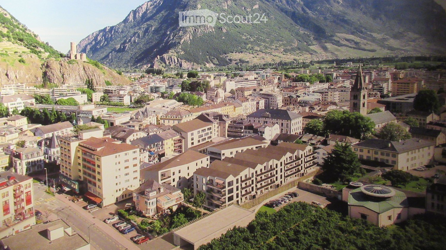 Aerial view of a town with many buildings, mountains in the background, and a clear sky.