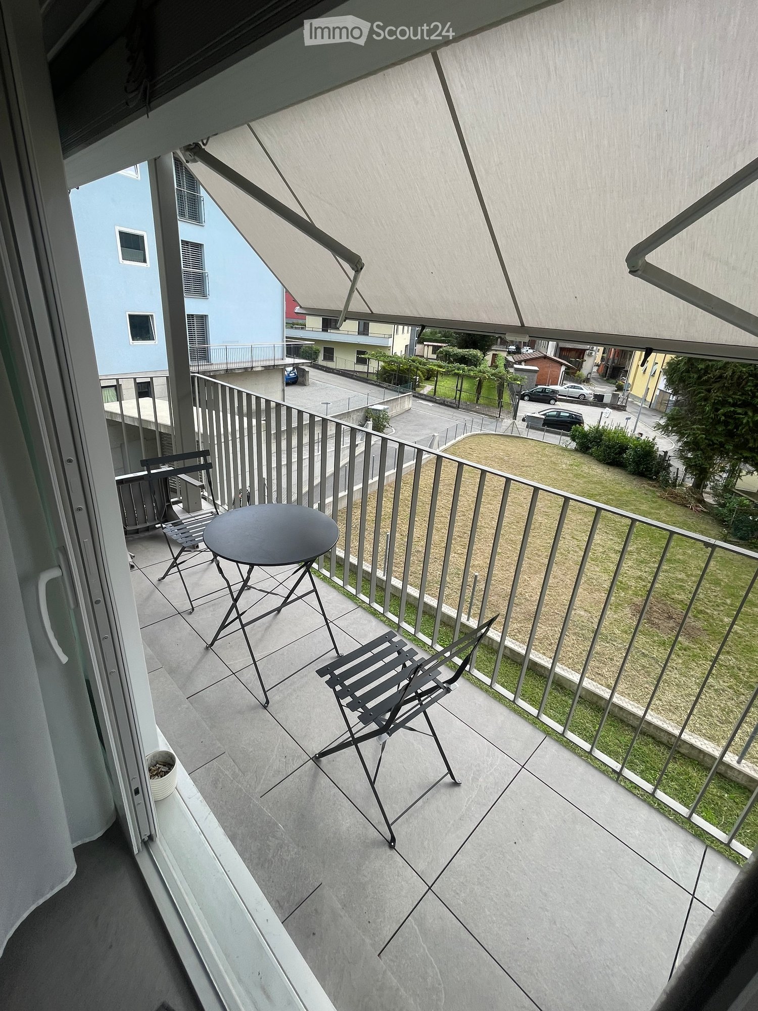 Balcony with tiled floor, metal railing, and outdoor furniture including a round table and two folding chairs.