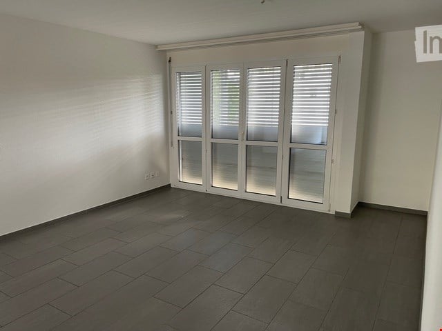Empty room with dark wooden flooring, white walls, and large white sliding doors with blinds.