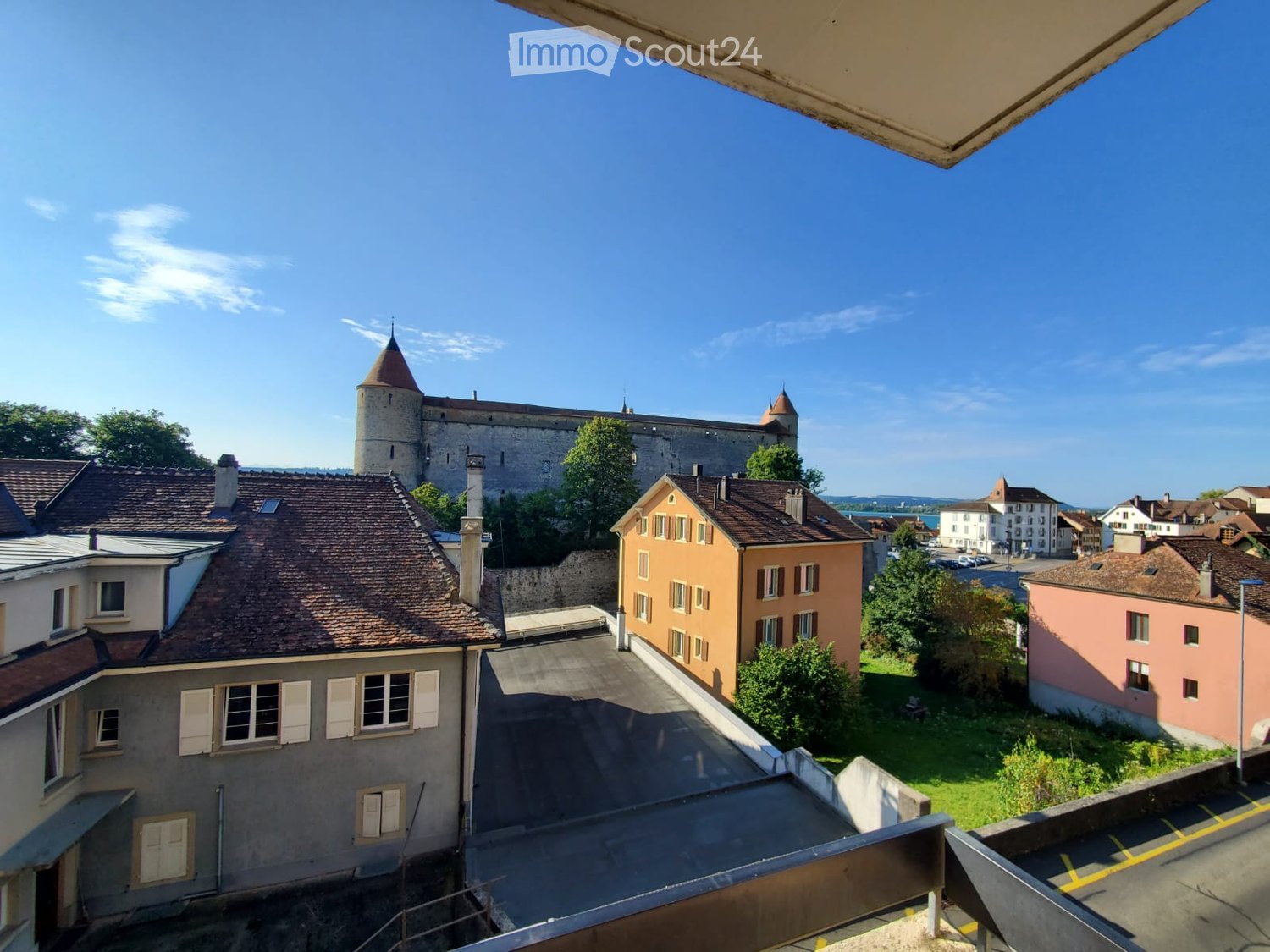 Balcony view overlooking a historic town with a castle, traditional houses, and a clear blue sky.