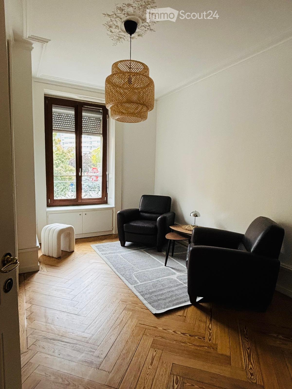 A room with two armchairs, a coffee table, a carpet, a floor lamp, and a window with view to outside.