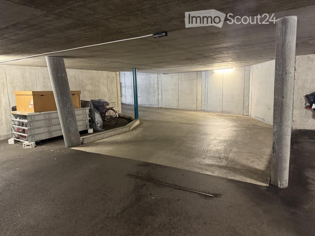 Underground garage with concrete pillars, storage items, and a bicycle. The space is mostly empty with a smooth concrete floor and walls.