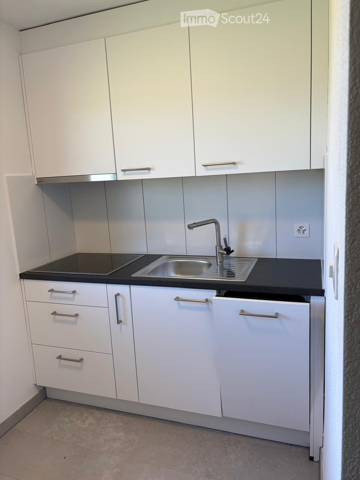 Modern kitchen with white cabinets, a stainless steel sink, and a black countertop.