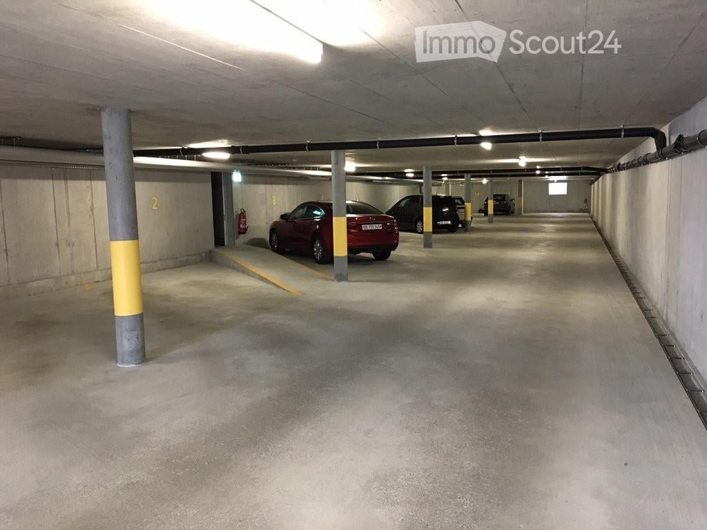 Underground parking area with several parked cars, concrete pillars, and fluorescent lighting.