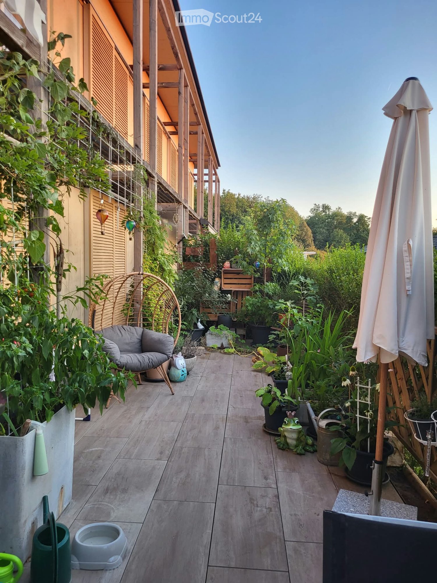 Balcony with tiled floor, sofa, umbrella, various potted plants, and decorative items.