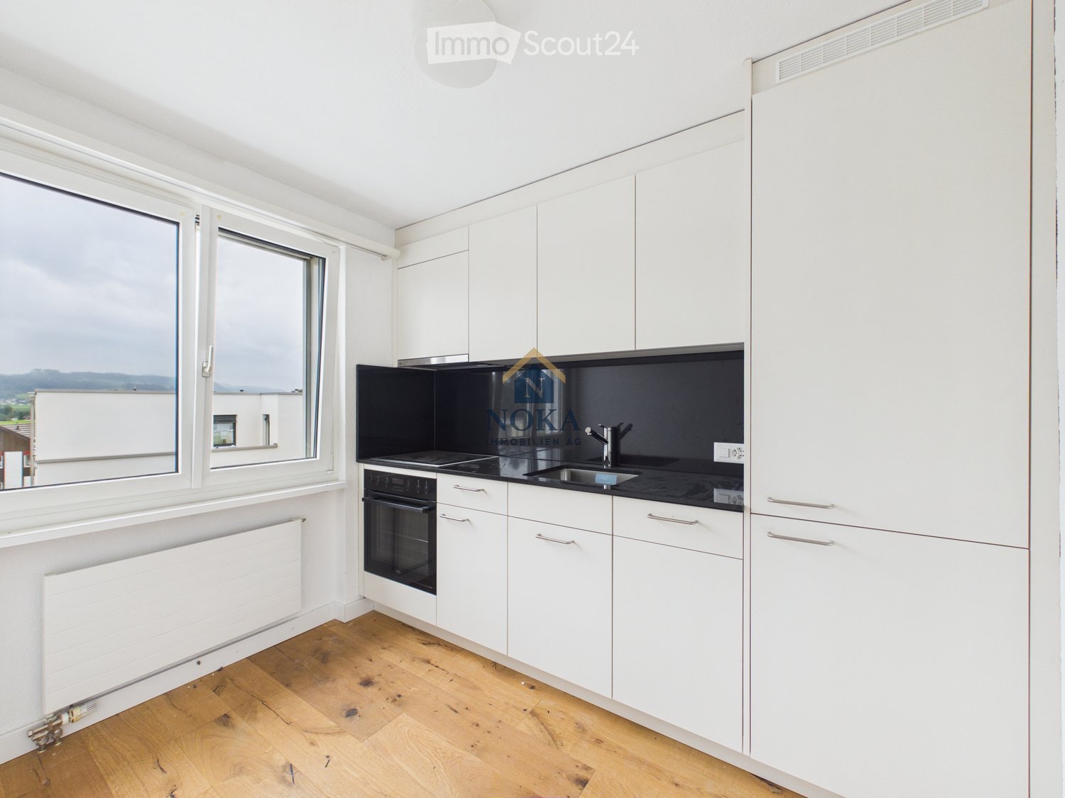 Modern kitchen with white cabinets, black countertops, wooden flooring, and large windows offering a view.