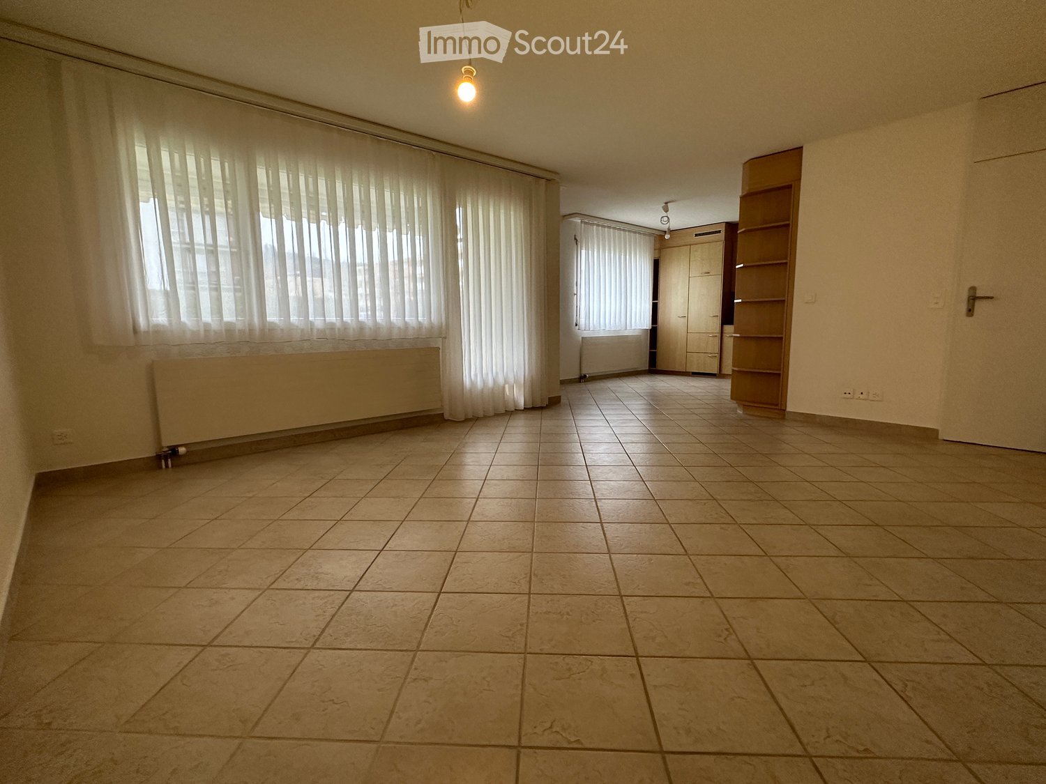 Empty room with tiled floor, large windows with white curtains, built-in closet, and radiator.