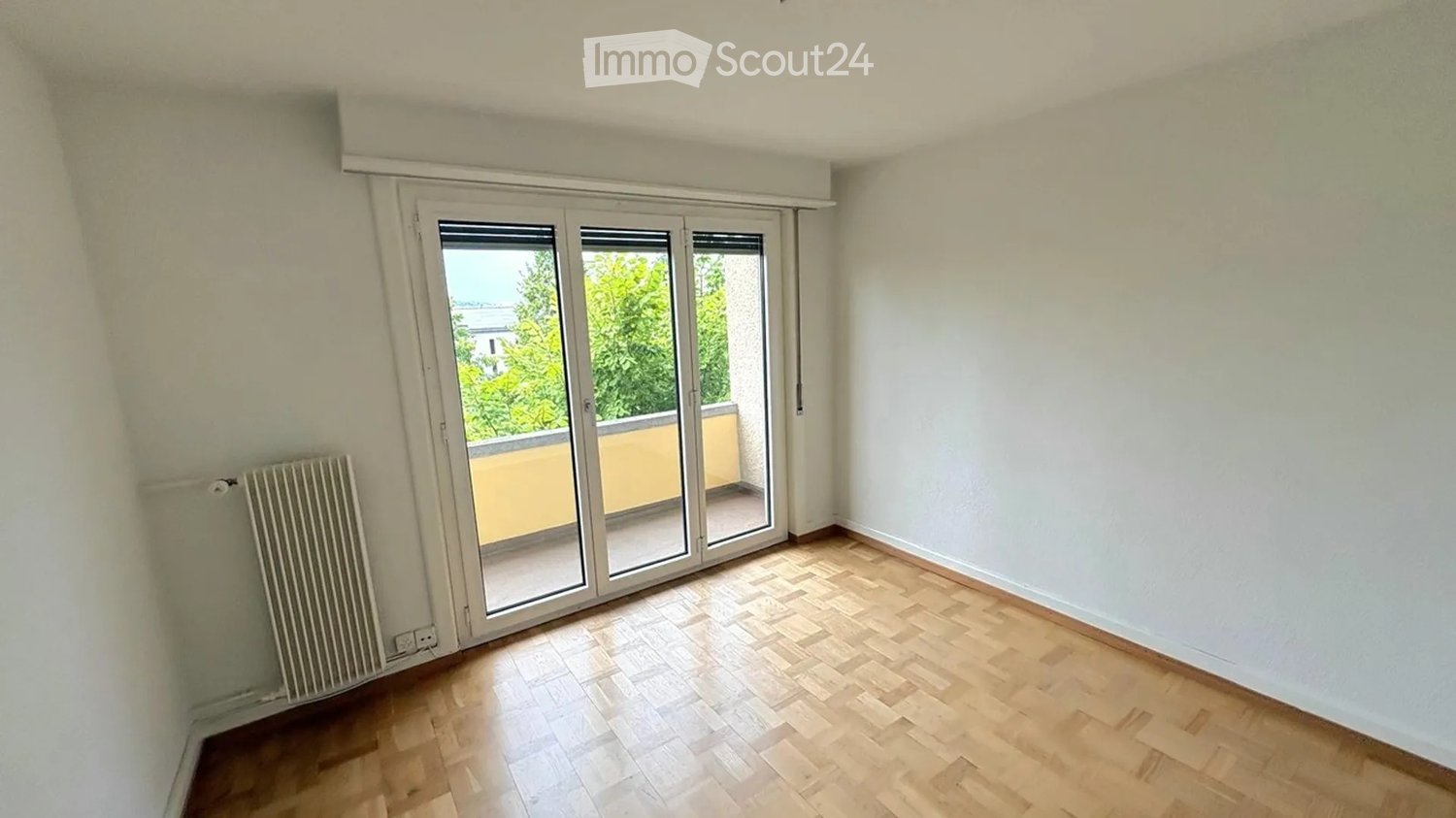 Empty room with wooden flooring, white walls, and large sliding glass doors leading to a balcony.