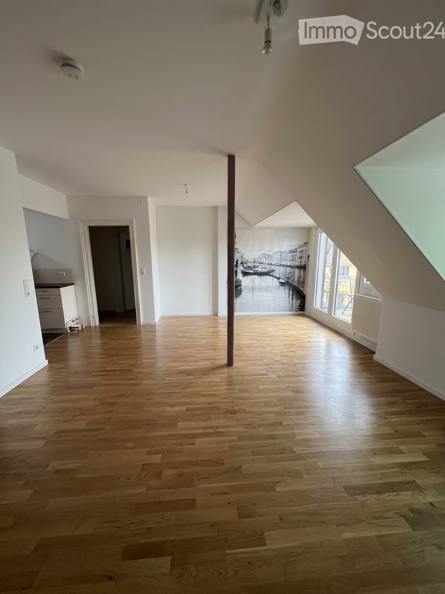 Empty room with wooden flooring, white walls, large windows, and a mural of a canal scene on one wall. No furniture or equipment is present.