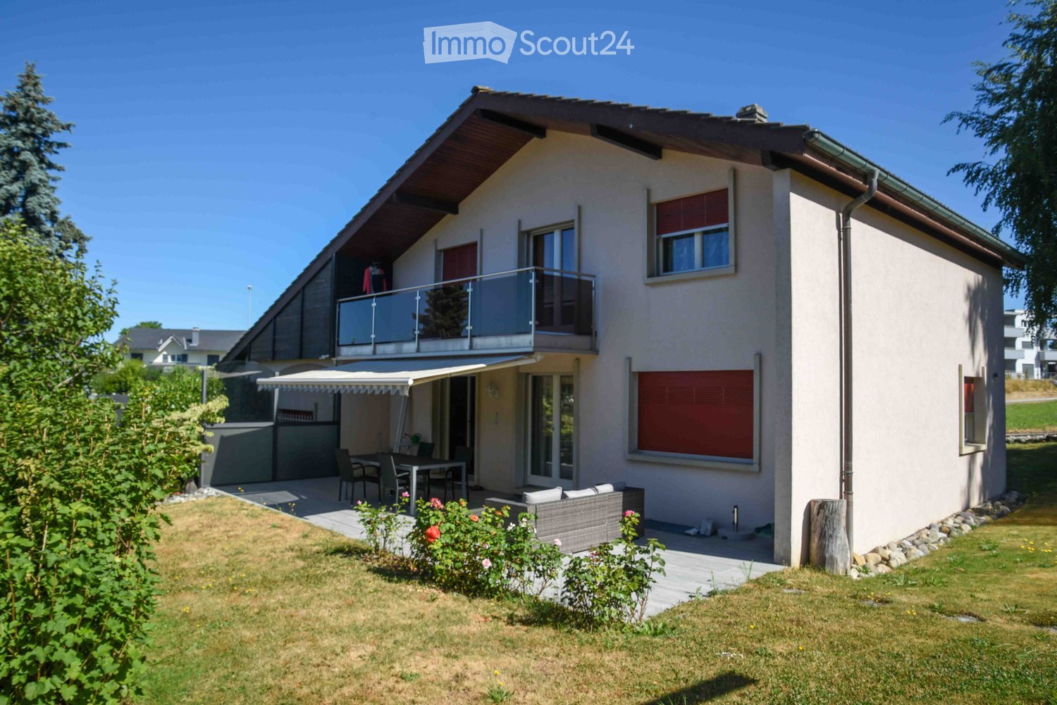 Two-story house with a modern design, featuring a balcony on the upper level, a patio with outdoor furniture, and a well-maintained garden.