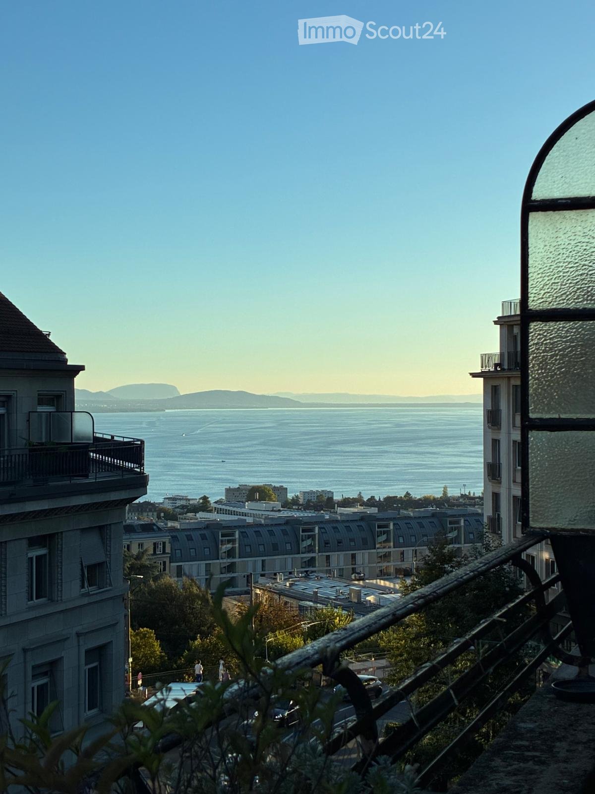 Balcony overlooking a cityscape with a body of water and distant mountains in the background.