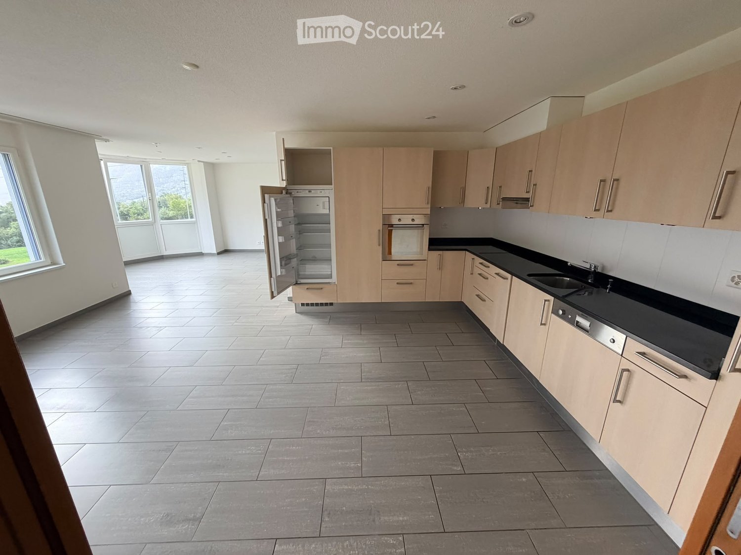 Modern kitchen with light wood cabinets, stainless steel appliances, and large windows letting in natural light.