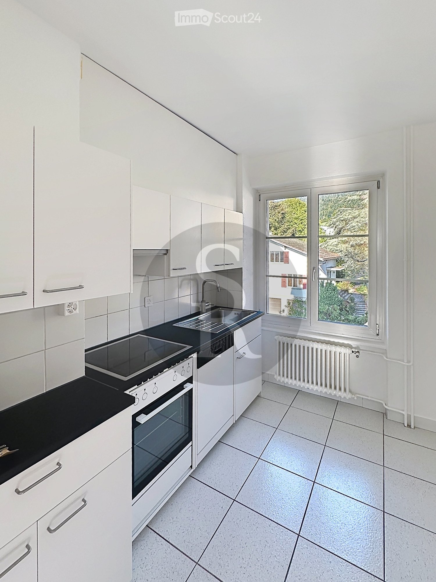 Modern kitchen with white cabinets, black countertop, stainless steel sink, oven, and radiator under window.