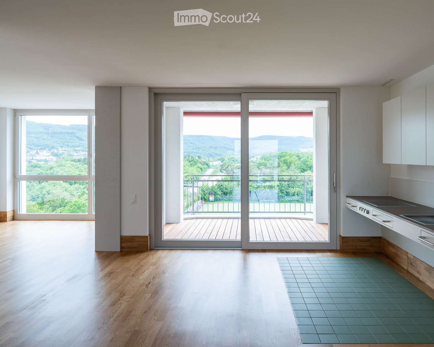 Bright, unfurnished room with wooden flooring, large windows, and a sliding glass door leading to a balcony with scenic views.