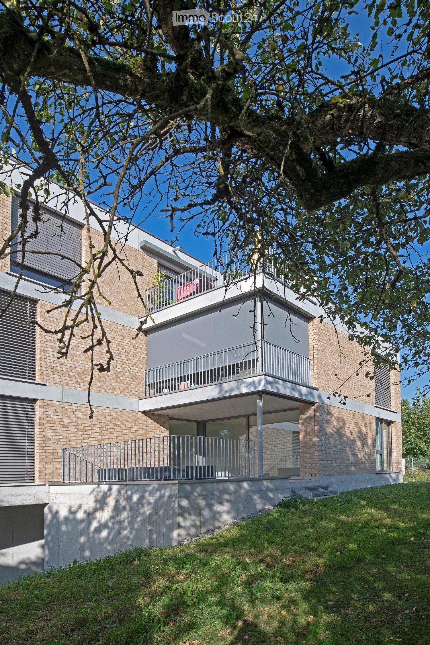 Modern two-story house with brick and white facade, large windows, and multiple balconies.