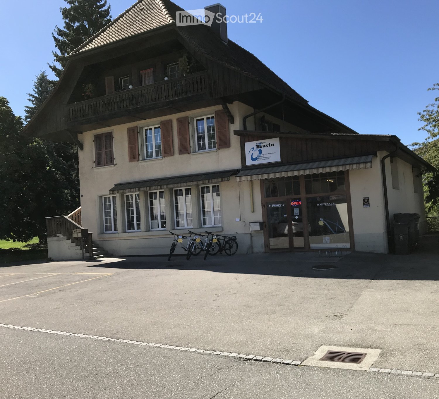 Two-story building with a balcony, multiple windows, and a storefront with glass doors and signage. Bicycles are parked in front.