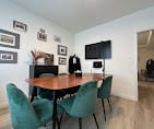 Dining room with a wooden dining table, four matching chairs, a mounted television, and several picture frames on the wall.
