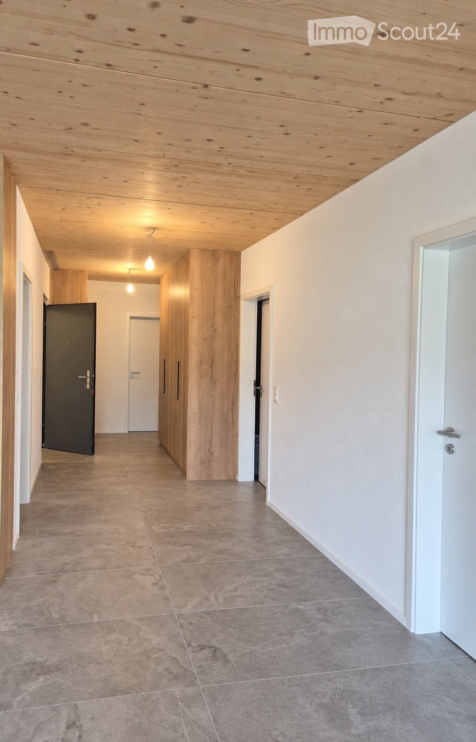 Empty hallway with wooden ceiling, tiled floor, white walls, and several doors leading to other rooms.