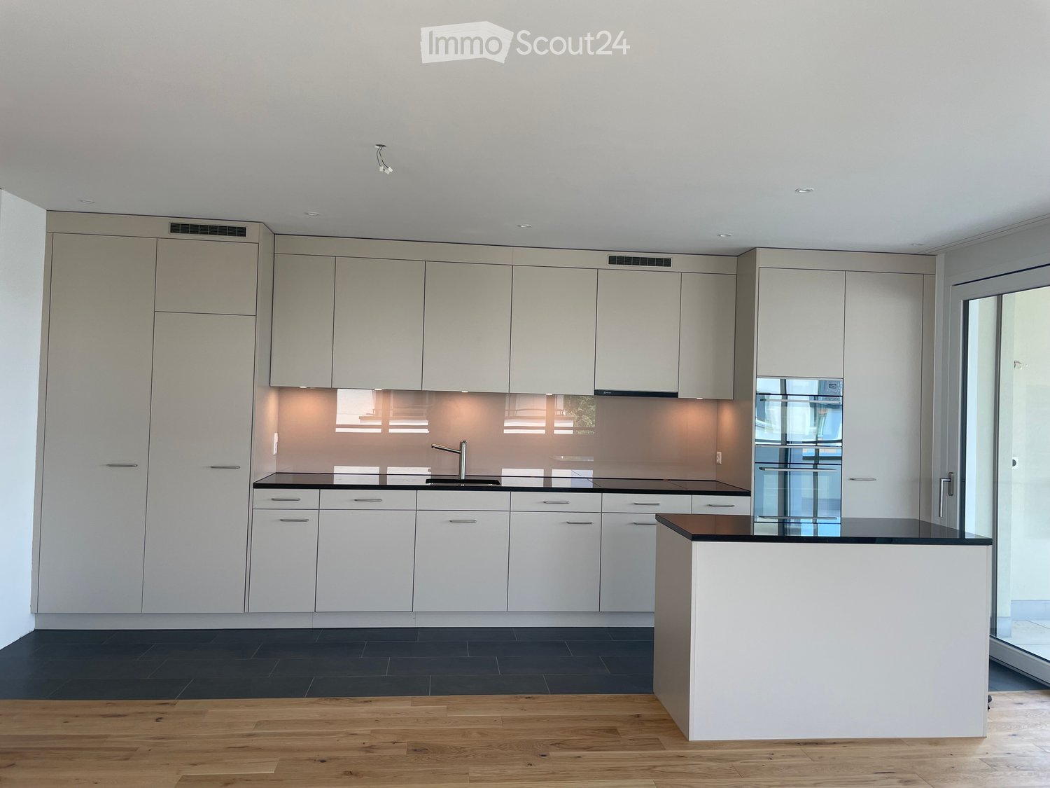 Modern kitchen with white cabinets, black countertops, and a central island. Features a sleek design with integrated lighting and a large window.