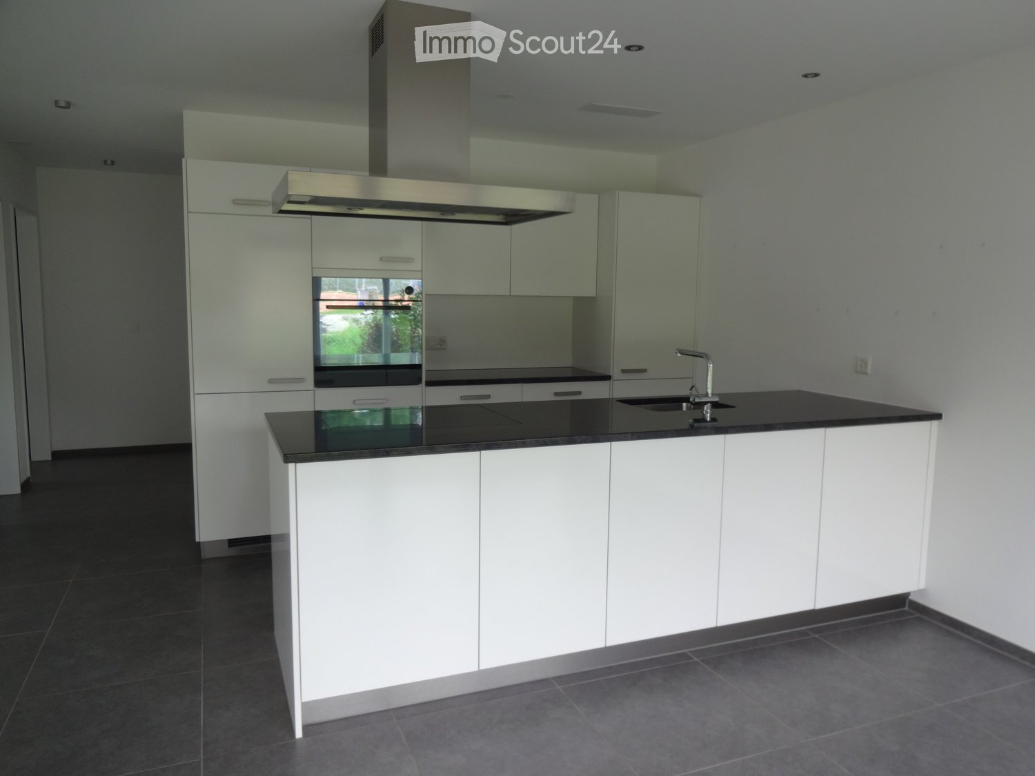 Modern kitchen with white cabinets, black countertops, and stainless steel appliances, including an oven and a sink with a modern faucet.