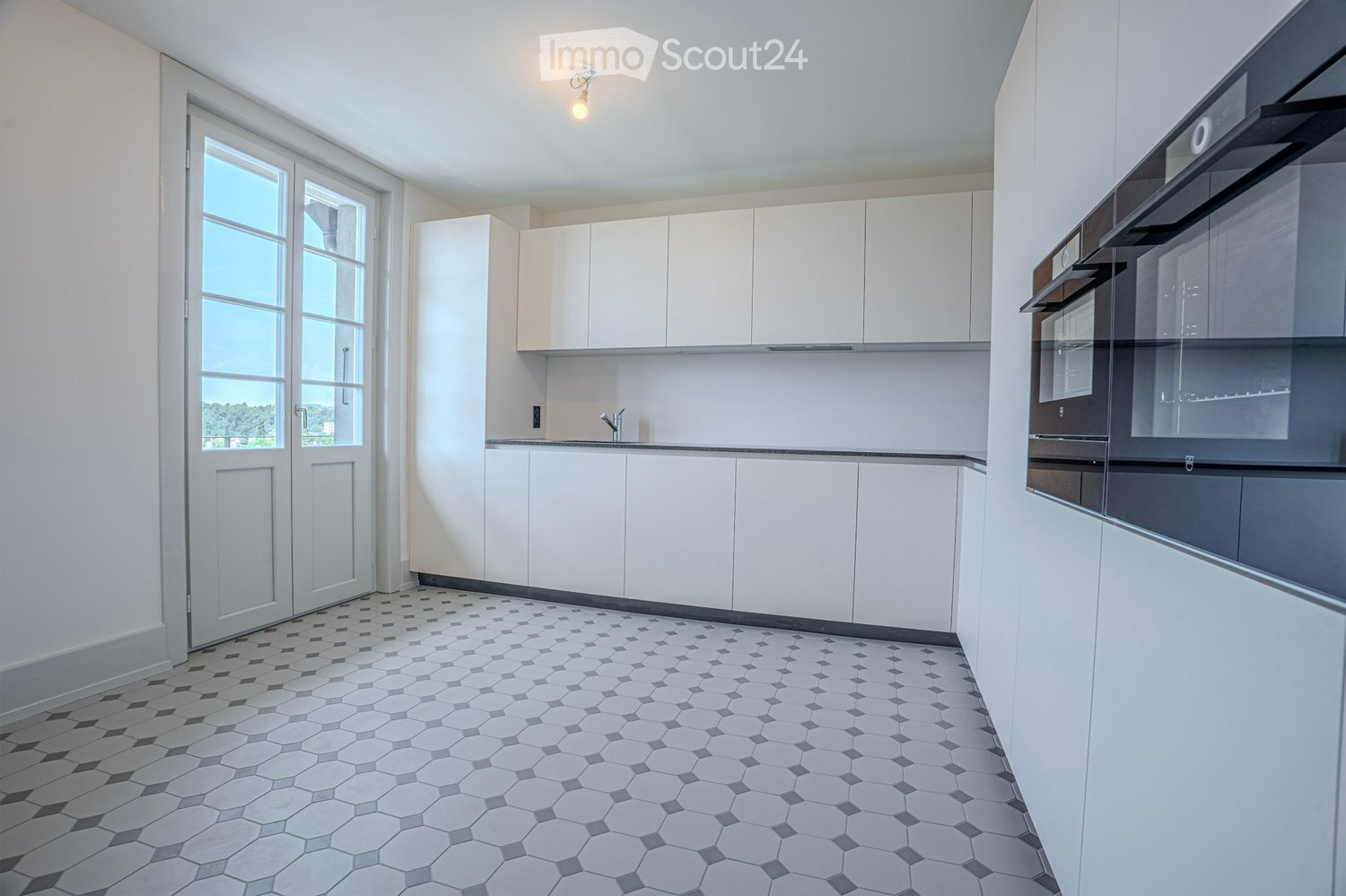 Modern kitchen with white cabinets, a built-in oven, and a sleek faucet. The floor features a geometric tile pattern in gray and white.