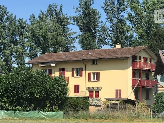 Two-story yellow house with red shutters, brown tiled roof, and a small balcony on the upper floor.
