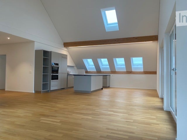 Bright, open kitchen with wooden flooring, modern grey cabinetry, and multiple skylights providing natural light. The space is completely empty, with no furniture or appliances visible.