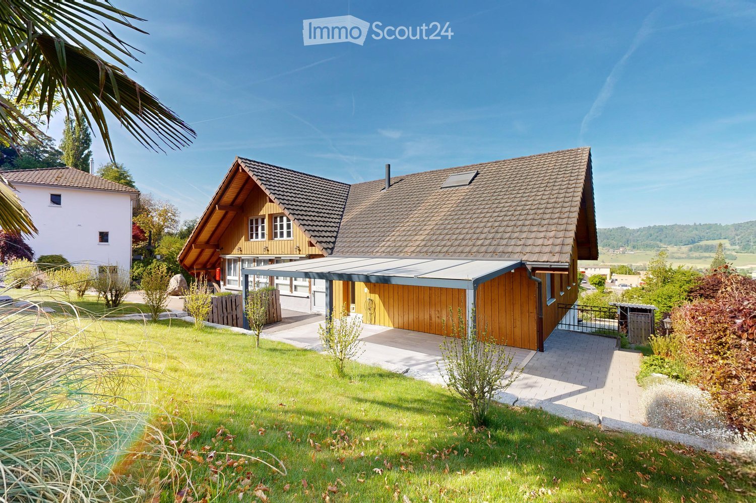 A two-story house with a tiled roof, wooden facade, and attached garage. The property features a well-maintained lawn, garden, and driveway.