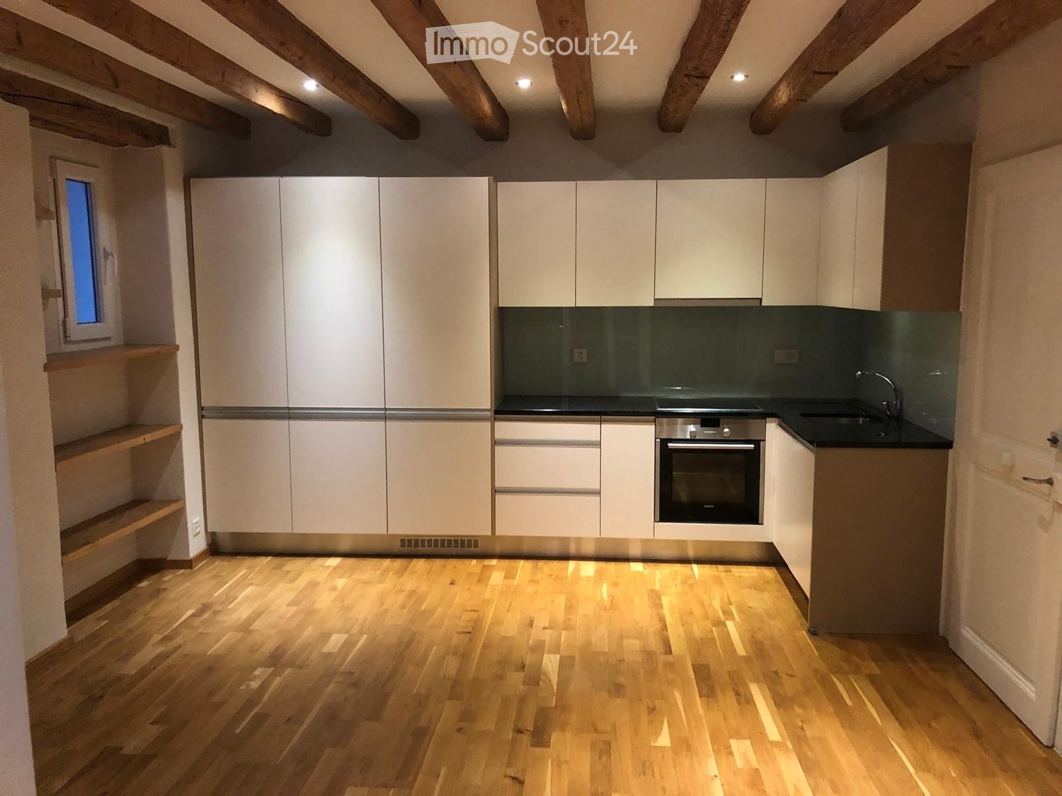Modern kitchen with white cabinets, stainless steel oven, and wooden flooring.