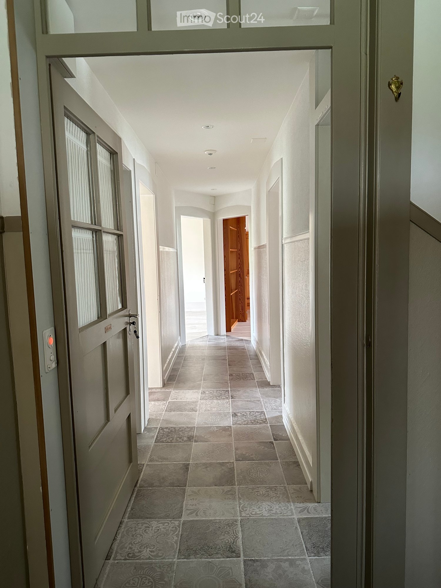 Corridor / Hallway. Empty hallway with tiled floor, white walls, and doors on both sides.