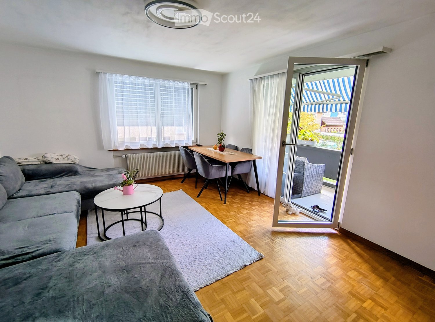 Living room with grey sofa, coffee table, dining table, chairs, and a view to a balcony.
