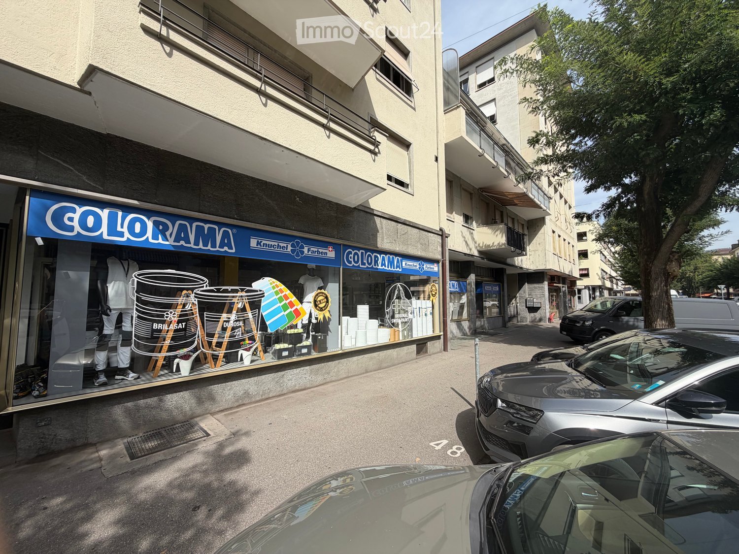 Multi-story building with storefront labeled "COLORAMA" displaying paint products and mannequins, with parked cars in front.