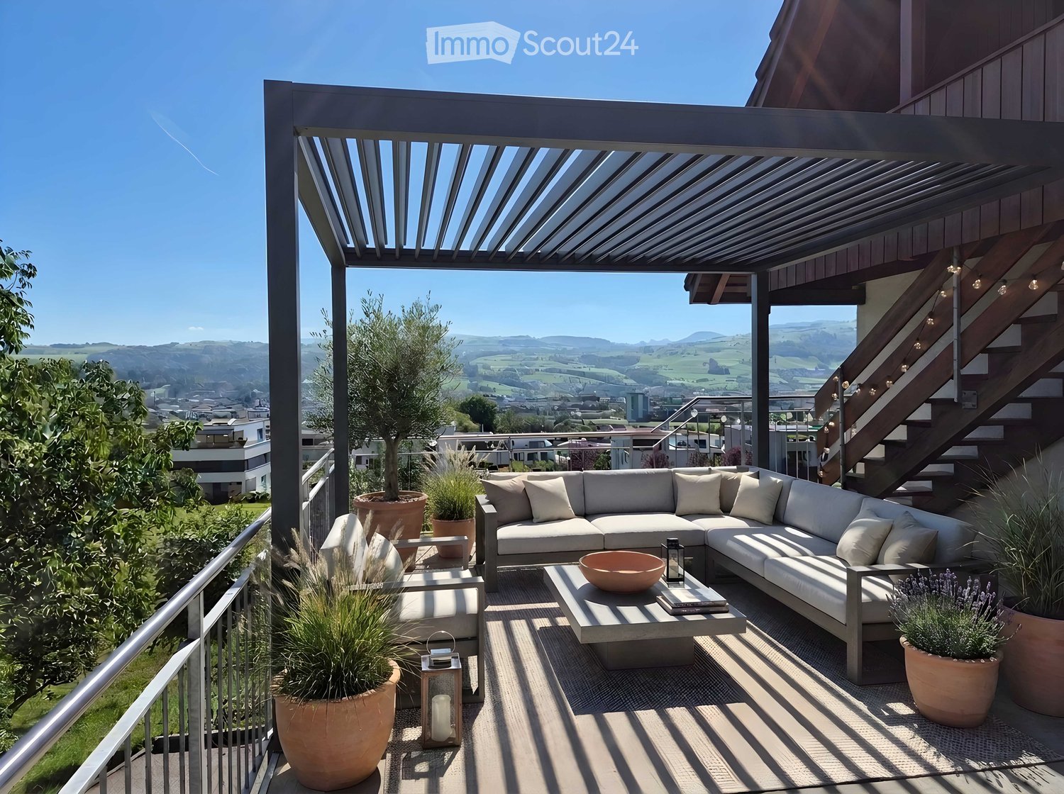 Modern outdoor patio with a sectional sofa, coffee table, decorative bowl, and lanterns, surrounded by potted plants and offering scenic views.