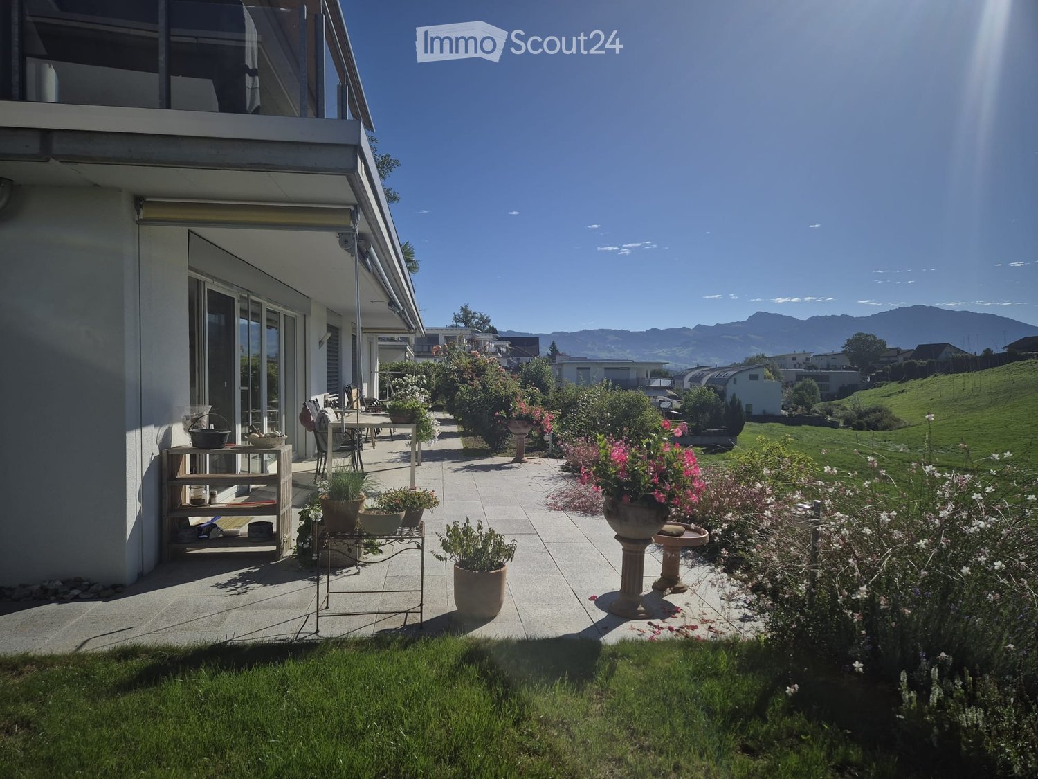 Well-maintained garden with a patio area, outdoor furniture, potted plants, and a scenic mountain view in the background.