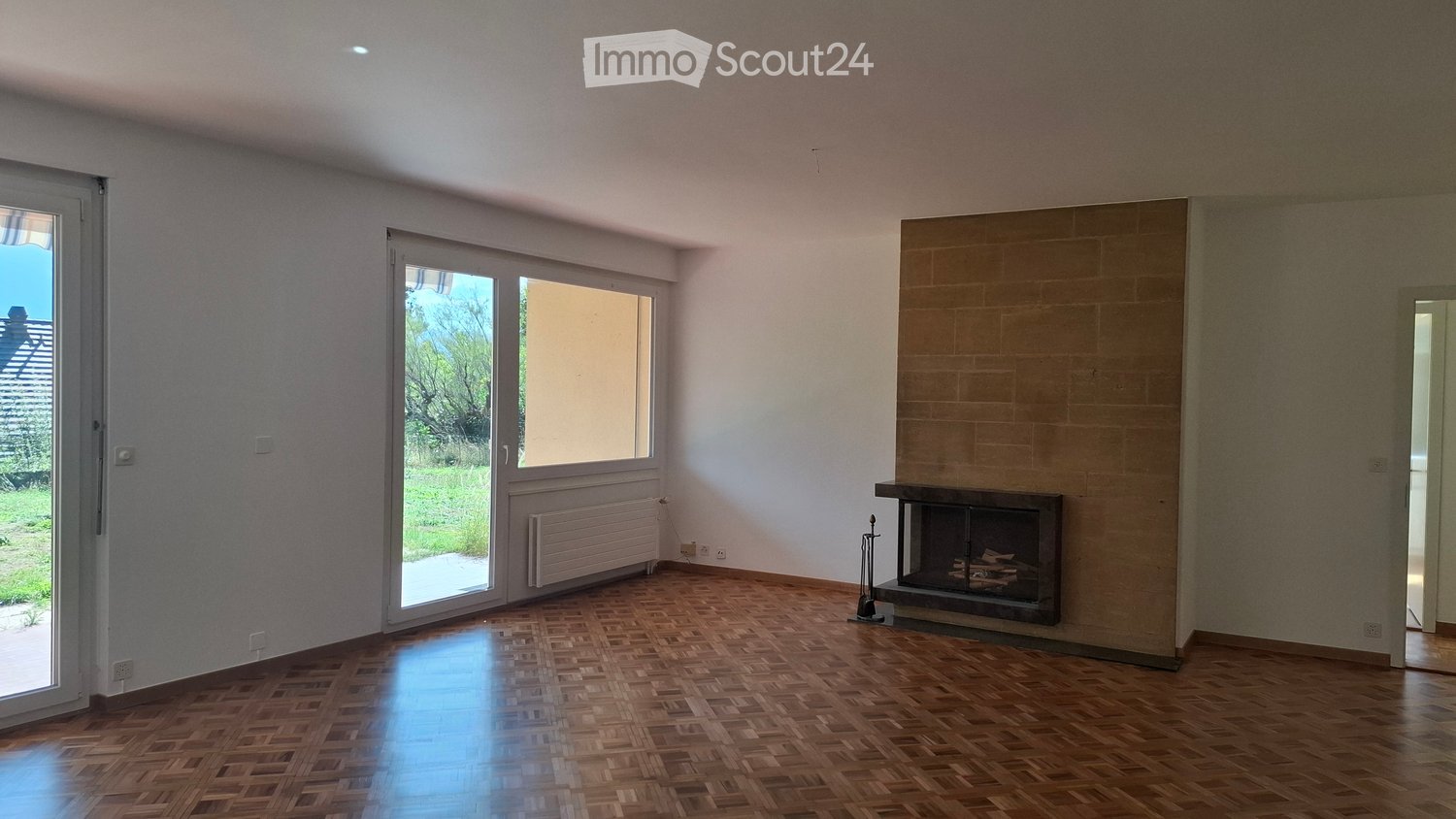 Empty room with wooden parquet flooring, white walls, large windows, and a fireplace with a tiled surround.